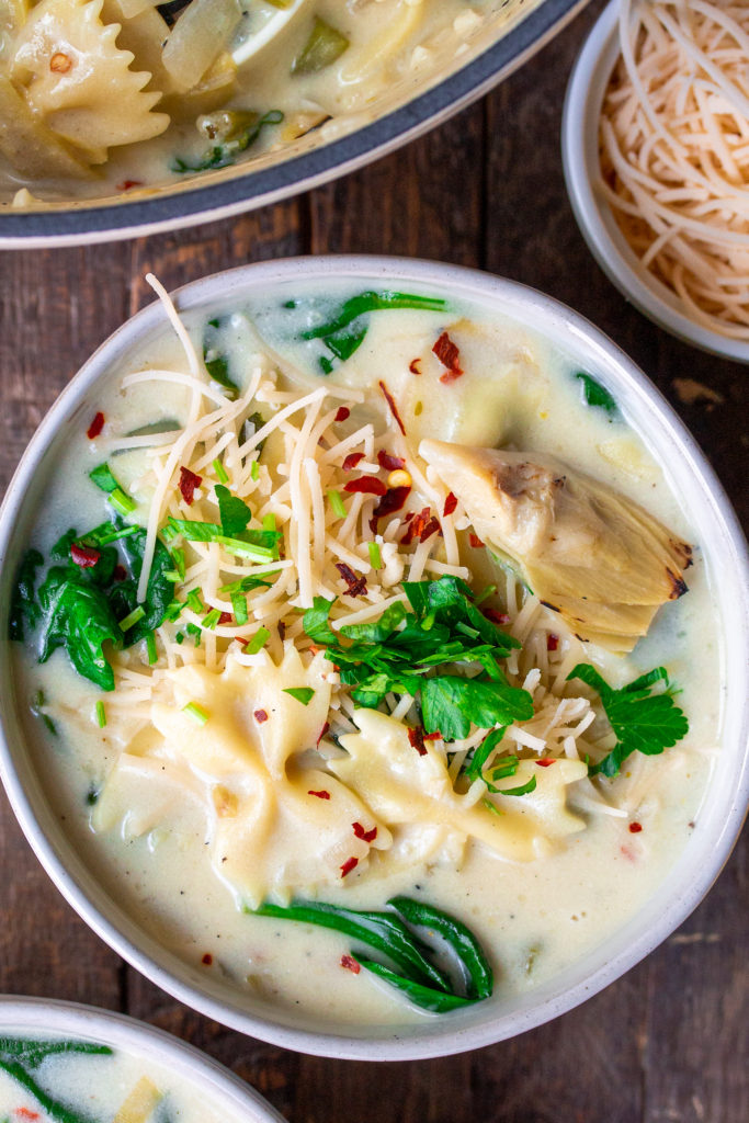 A pot of creamy soup with noodles, spinach, and artichoke hearts