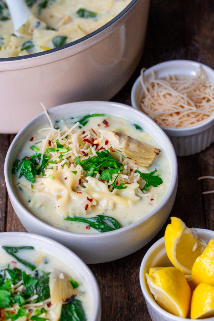 A pot of creamy soup with noodles, spinach, and artichoke hearts