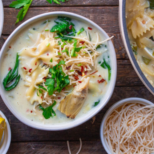 A pot of creamy soup with noodles, spinach, and artichoke hearts