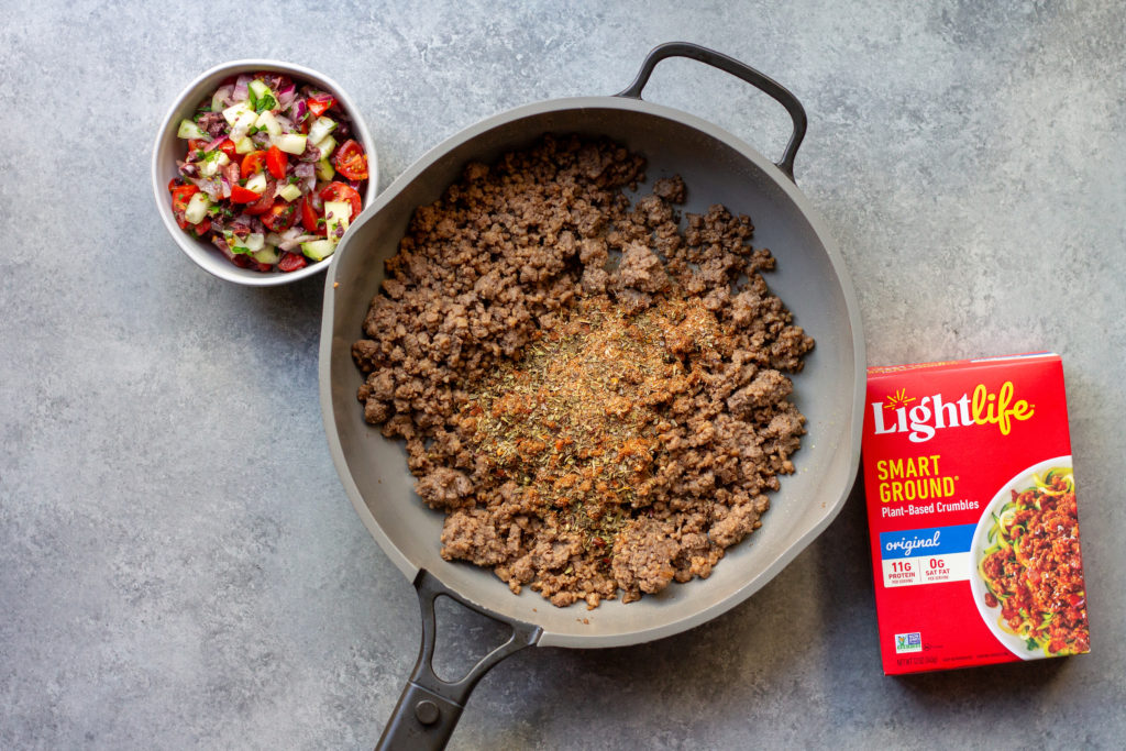 A step-by-step image of assembling the Vegan Mediterranean-Inspired Taco with pita bread, starting with adding Lightlife Smart Ground.