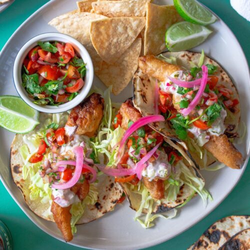 Golden crispy beer-battered vegan fish tacos topped with creamy chipotle sauce and fresh pico de Gallo.