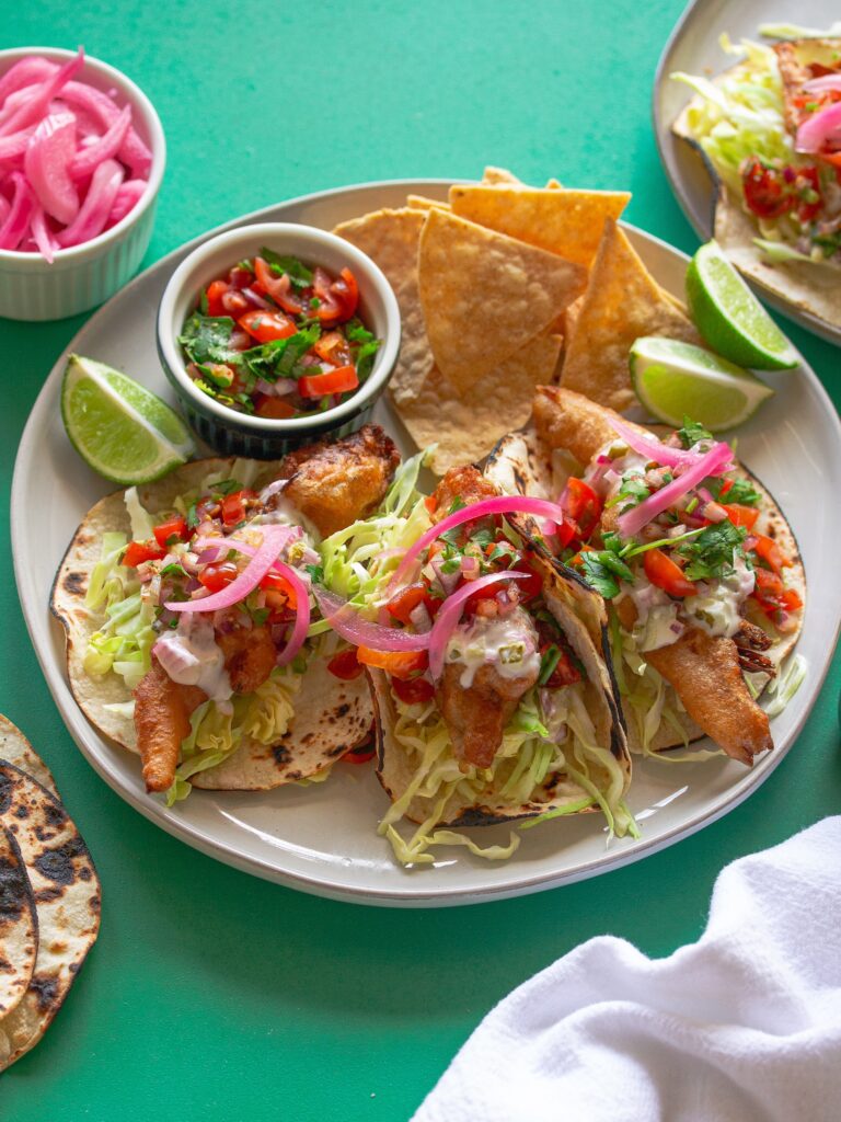 Golden crispy beer-battered vegan fish tacos topped with creamy chipotle sauce and fresh pico de Gallo.