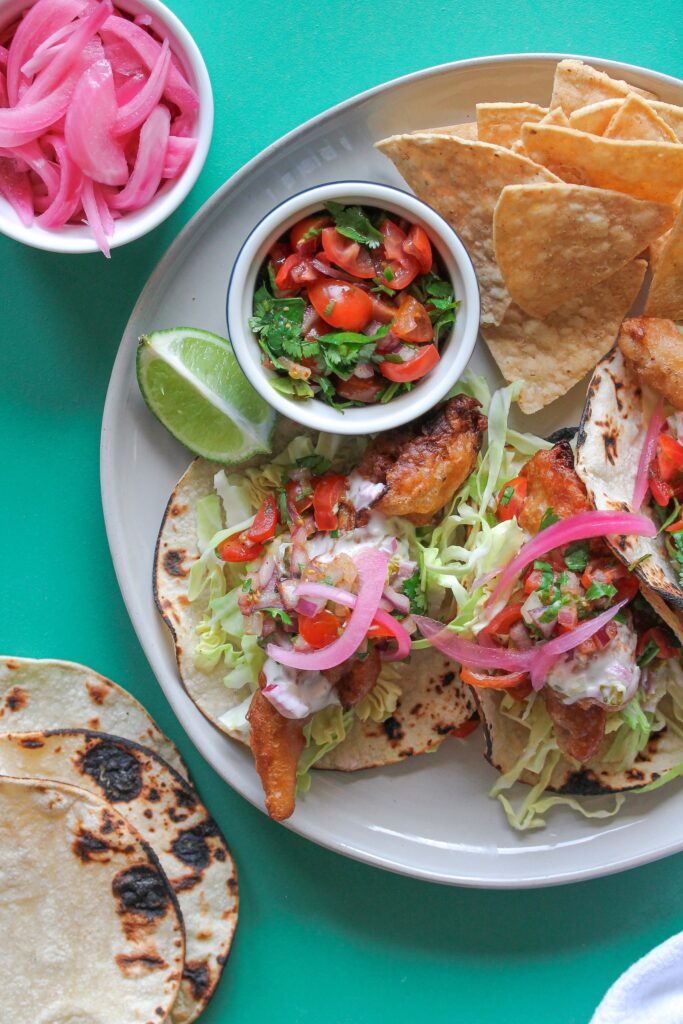 Golden crispy beer-battered vegan fish tacos topped with creamy chipotle sauce and fresh pico de Gallo.
