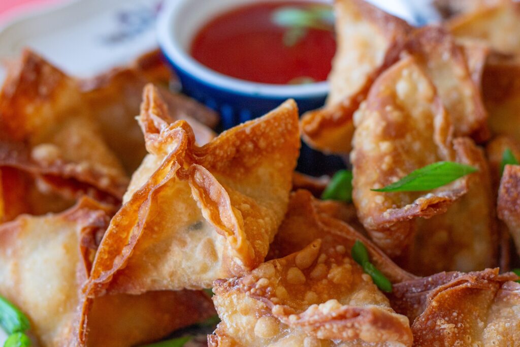 Completed Vegan Crab Rangoon, garnished with chopped chives, and served with sweet chili sauce.