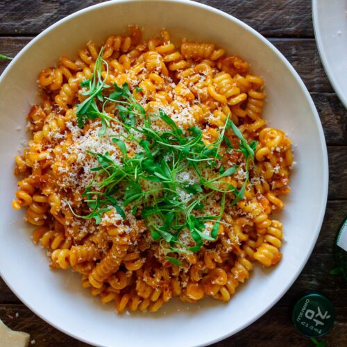 Final presentation of the Creamy Gochujang Pasta, garnished with vegan parmesan shreds and fresh cilantro micro greens.