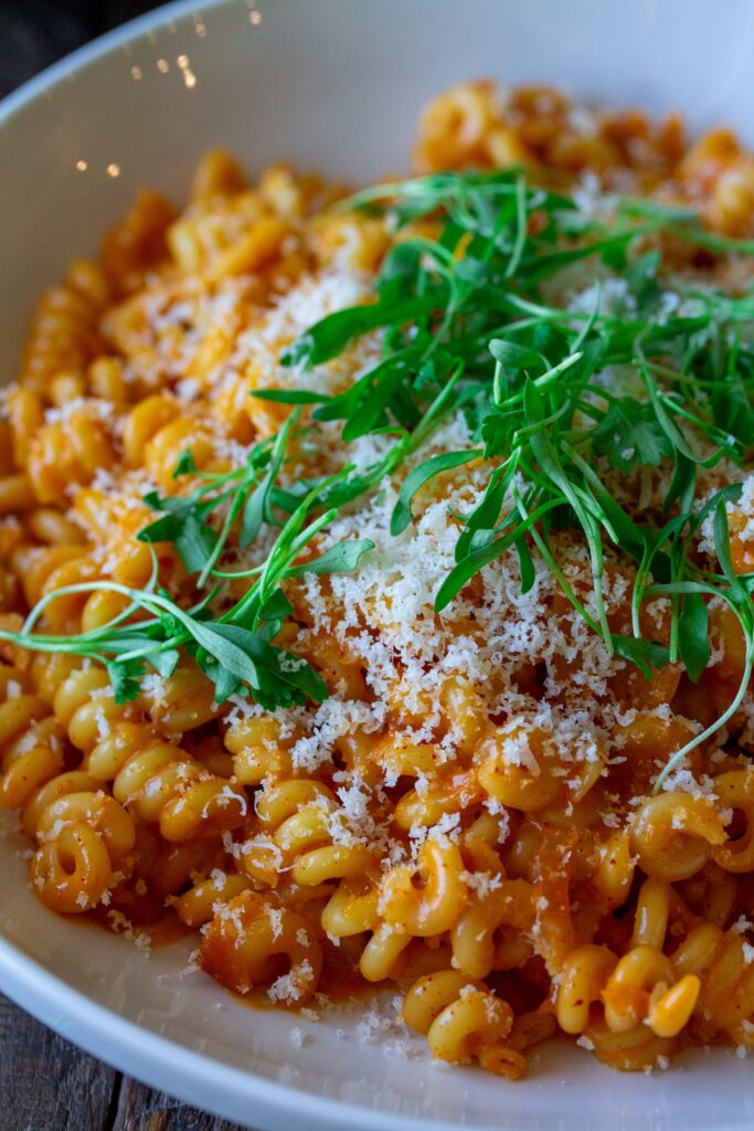 Final presentation of the Creamy Gochujang Pasta, garnished with vegan parmesan shreds and fresh cilantro micro greens 