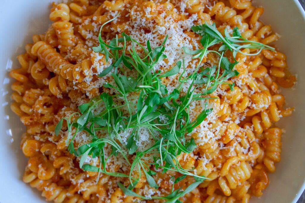 Final presentation of the Creamy Gochujang Pasta, garnished with vegan parmesan shreds and fresh cilantro micro greens 