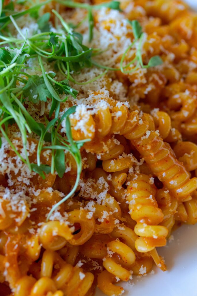 Final presentation of the Creamy Gochujang Pasta, garnished with vegan parmesan shreds and fresh cilantro micro greens 
