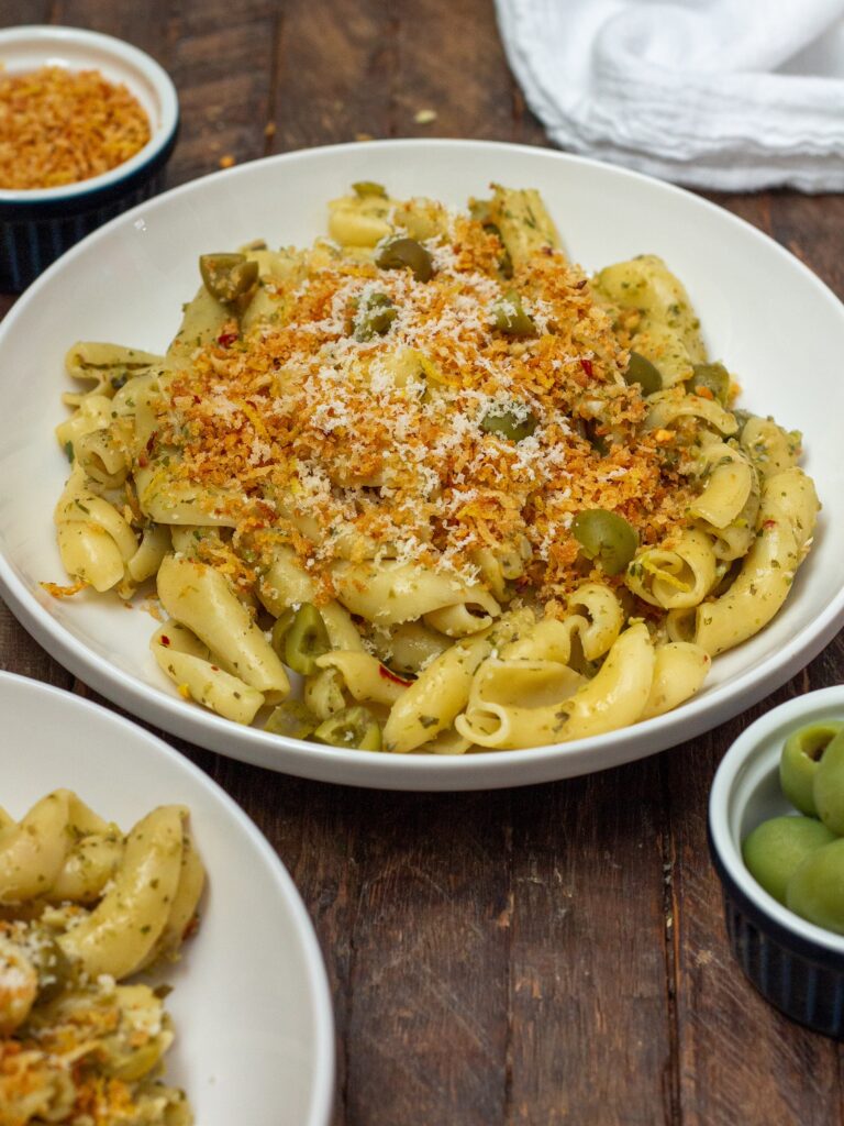 A plate of Vegan Green Olive Pasta garnished with vegan parmesan and fresh minced parsley