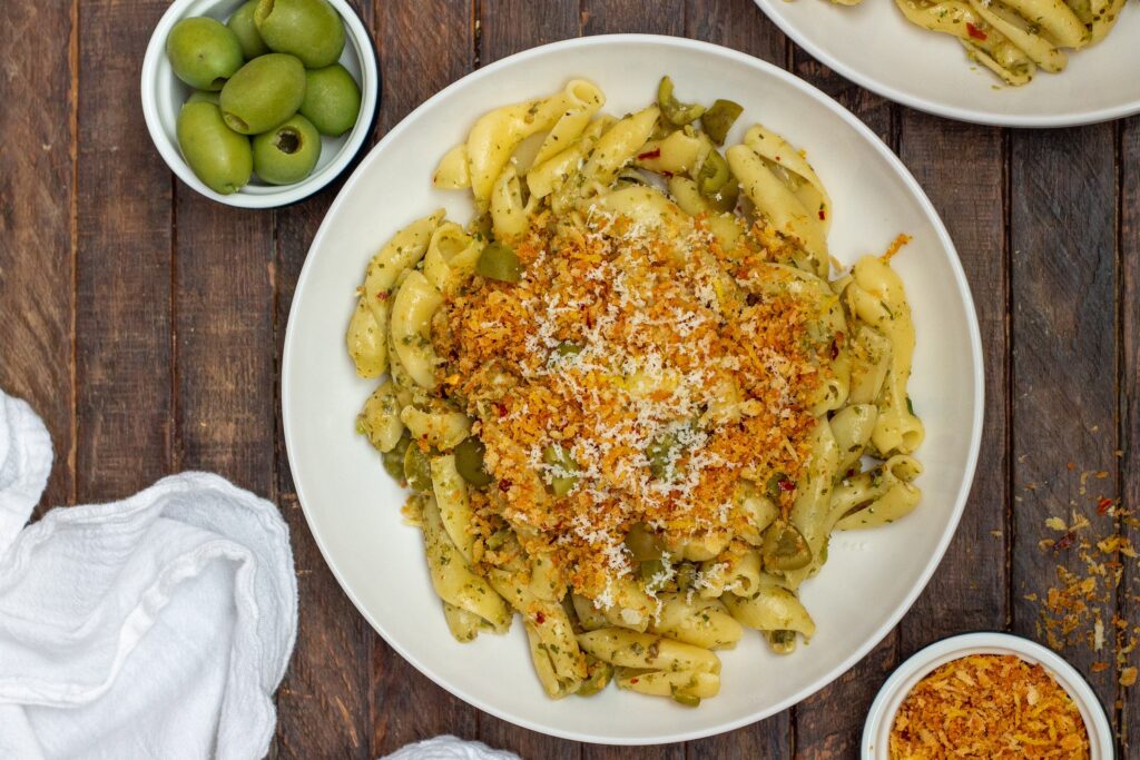 A plate of Vegan Green Olive Pasta garnished with vegan parmesan and fresh minced parsley