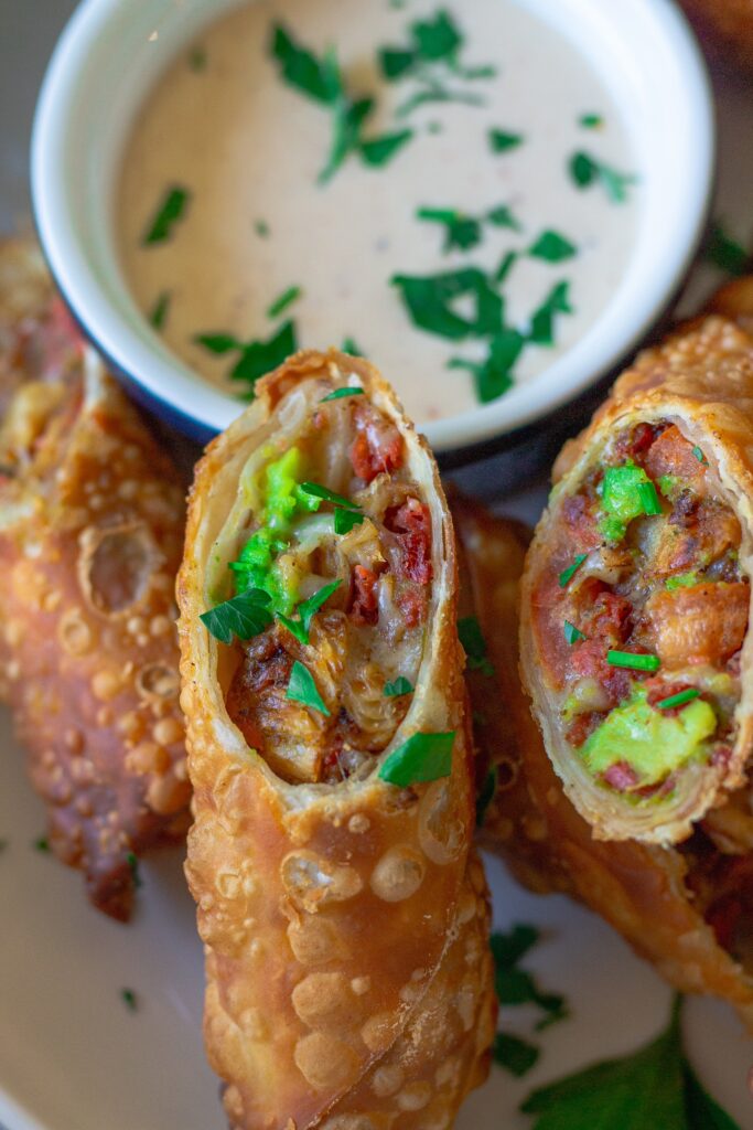 Close-up of a cut-open avocado club egg roll showcasing the flavorful filling of seasoned vegan chicken, avocado, tomatoes, and vegan cheese.