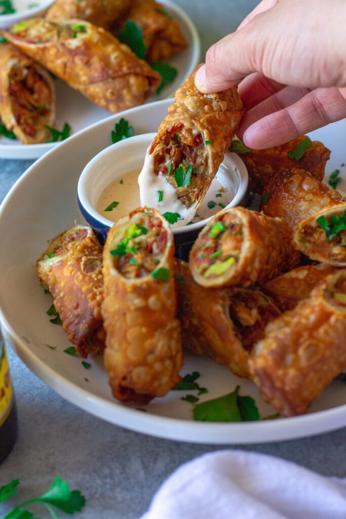 Close-up of a cut-open avocado club egg roll showcasing the flavorful filling of seasoned vegan chicken, avocado, tomatoes, and vegan cheese.