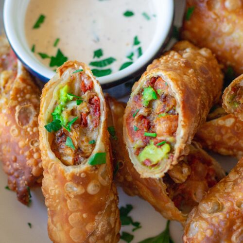 Close-up of a cut-open avocado club egg roll showcasing the flavorful filling of seasoned vegan chicken, avocado, tomatoes, and vegan cheese.