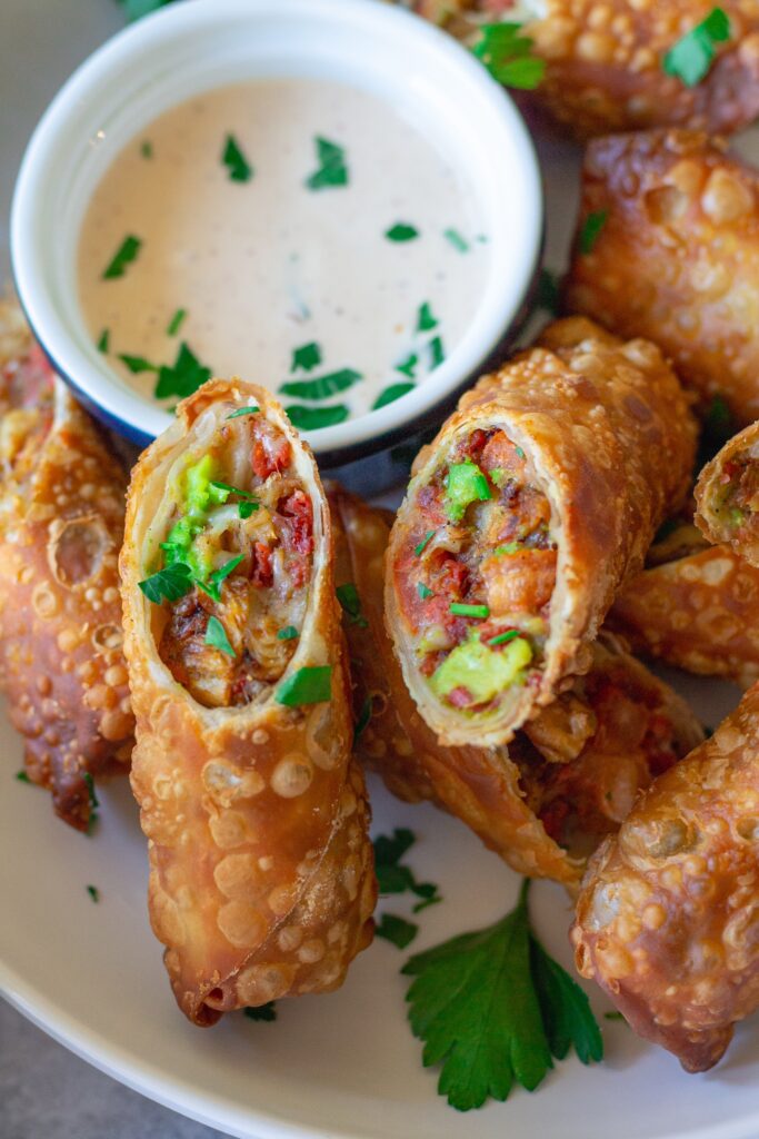 Close-up of a cut-open avocado club egg roll showcasing the flavorful filling of seasoned vegan chicken, avocado, tomatoes, and vegan cheese.