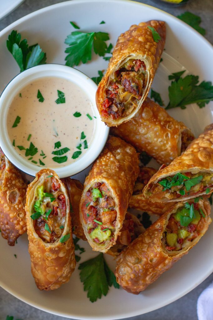 Close-up of a cut-open avocado club egg roll showcasing the flavorful filling of seasoned vegan chicken, avocado, tomatoes, and vegan cheese.