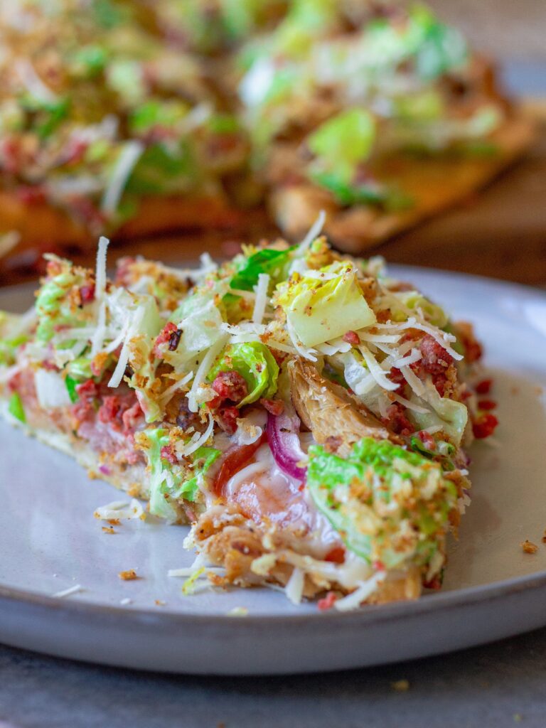 Sliced Vegan Chicken Caesar Salad Pizza served on a wooden board with a side of lemony breadcrumbs