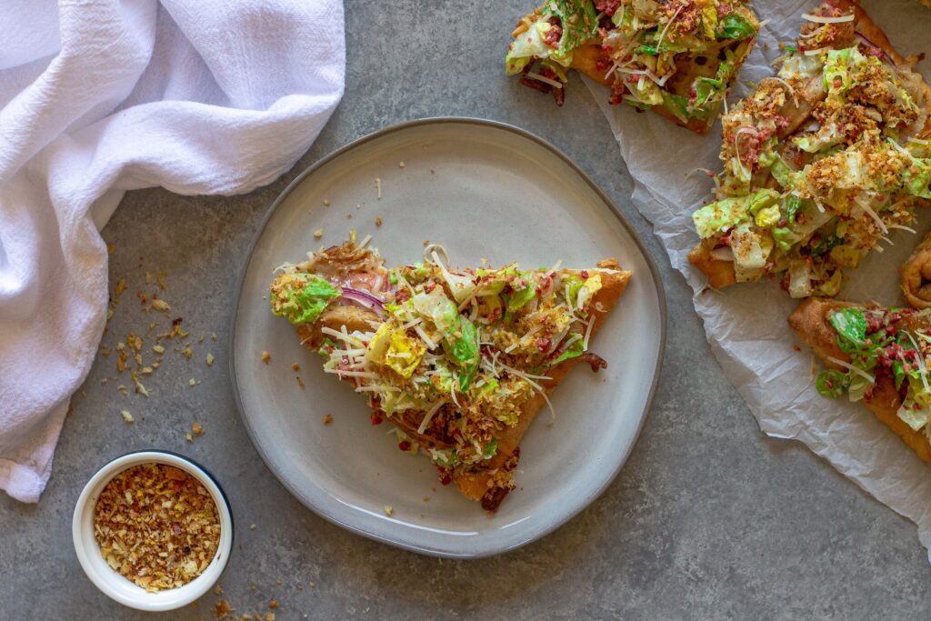 Sliced Vegan Chicken Caesar Salad Pizza served on a wooden board with a side of lemony breadcrumbs