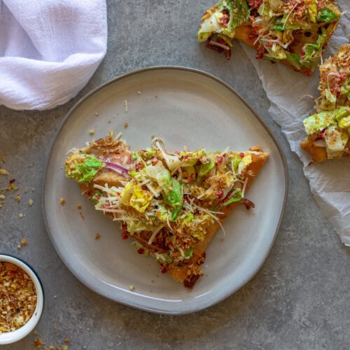 Sliced Vegan Chicken Caesar Salad Pizza served on a wooden board with a side of lemony breadcrumbs
