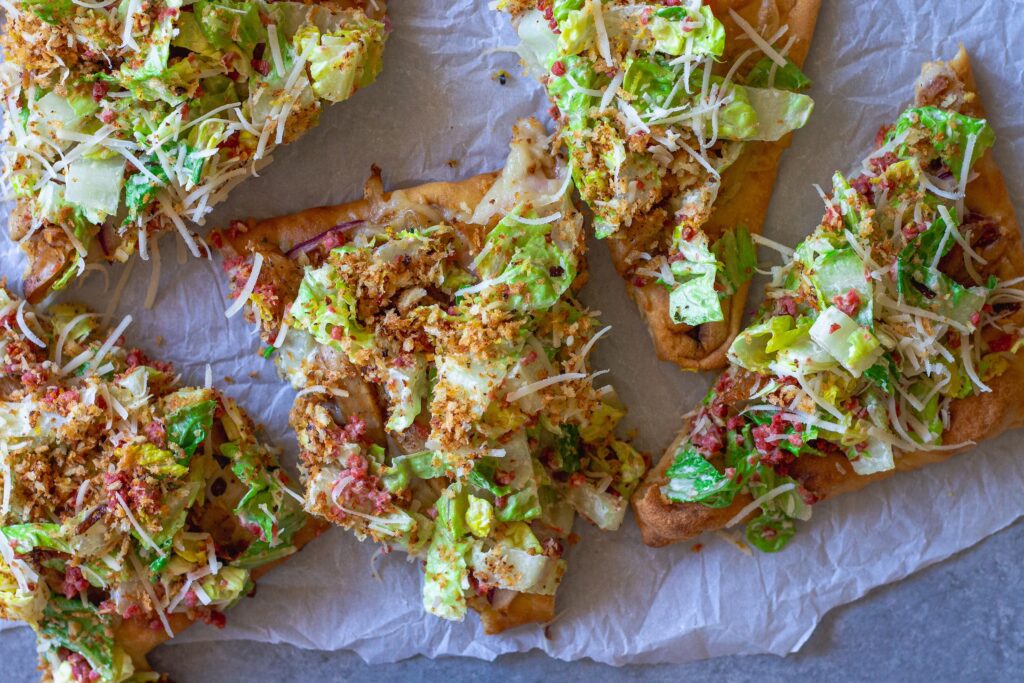 Sliced Vegan Chicken Caesar Salad Pizza served on a wooden board with a side of lemony breadcrumbs