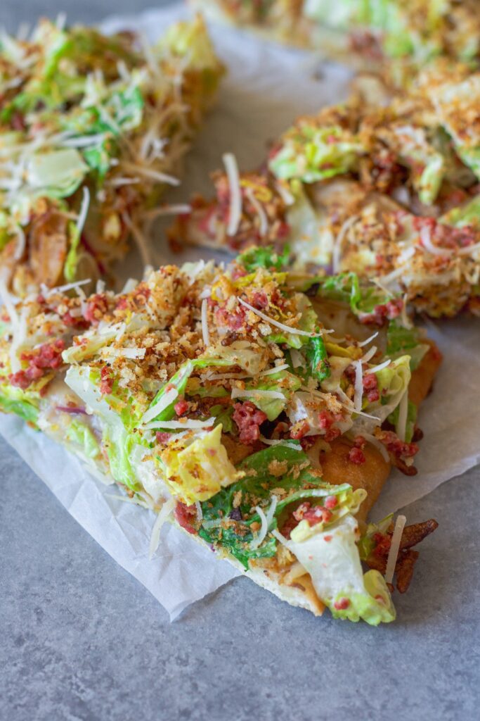 Sliced Vegan Chicken Caesar Salad Pizza served on a wooden board with a side of lemony breadcrumbs