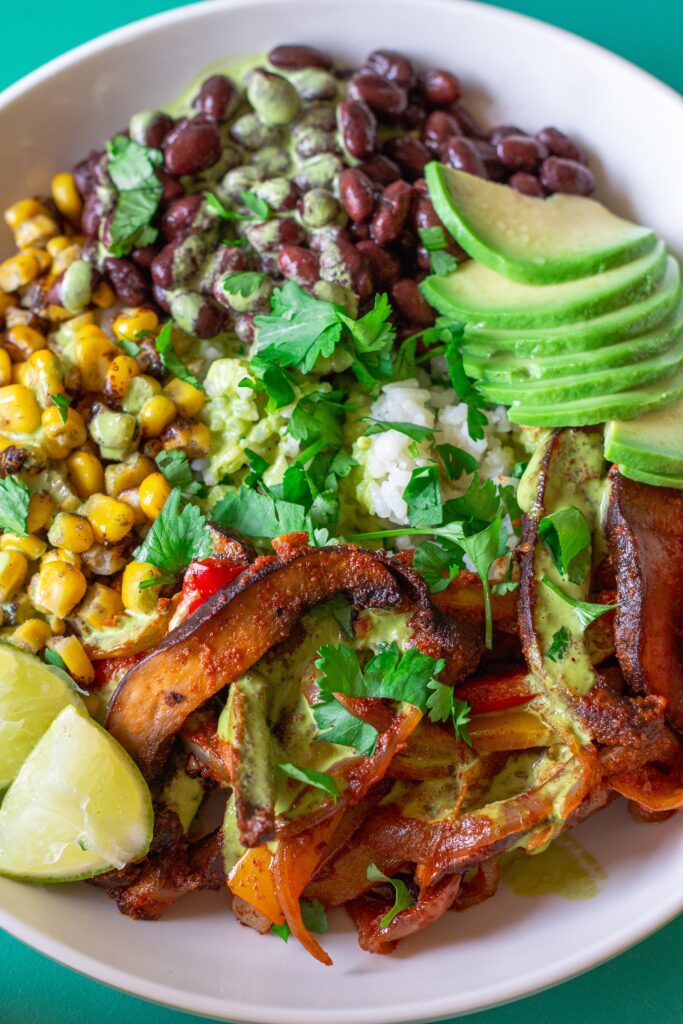 Vegan Mushroom Fajita Bowl with cilantro lime rice, roasted portobello mushrooms, black beans, corn, avocado, and drizzled with cilantro lime crema.