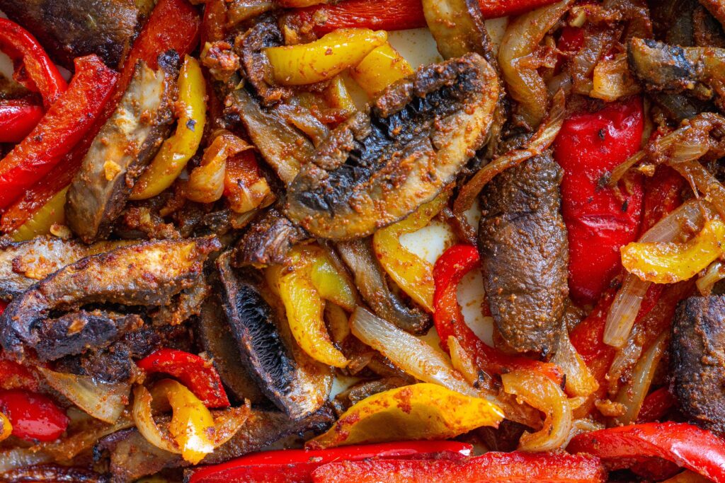 Vegetables seasoned with spices and avocado oil roasting in the oven for Vegan Mushroom Fajita Bowls.