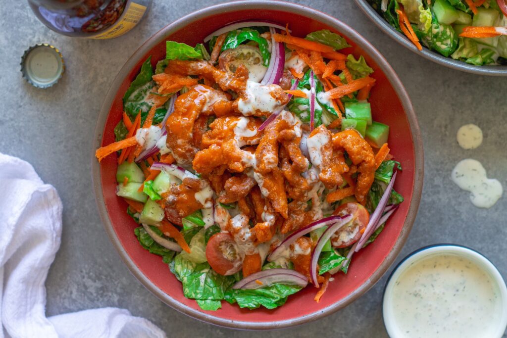 Close-up of a serving of Crispy Vegan Buffalo Chicken Salad in a bowl, garnished with fresh dill.