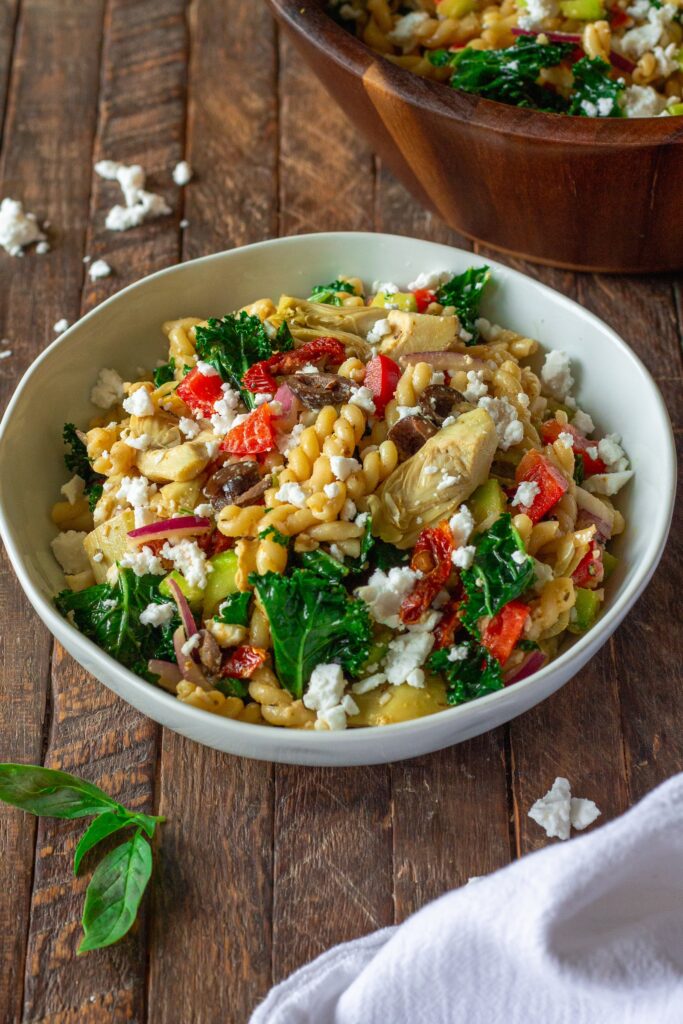 Finished Vegan Mediterranean Pasta Salad garnished with vegan feta crumbles and fresh basil leaves.