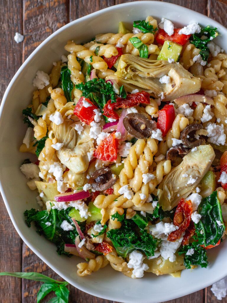 Finished Vegan Mediterranean Pasta Salad garnished with vegan feta crumbles and fresh basil leaves.