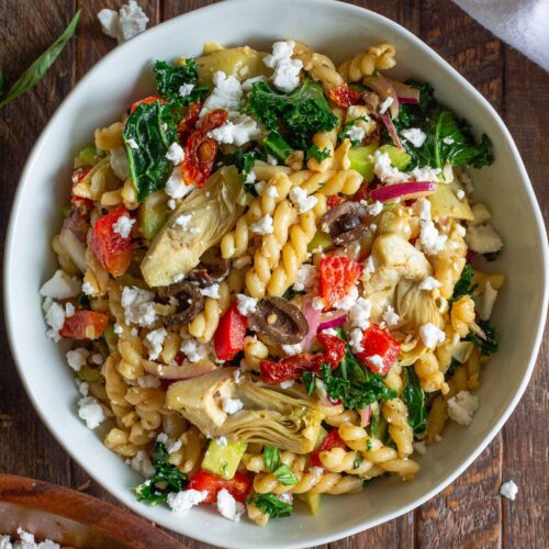 Finished Vegan Mediterranean Pasta Salad garnished with vegan feta crumbles and fresh basil leaves.