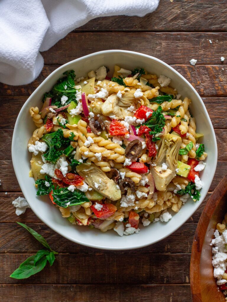 Finished Vegan Mediterranean Pasta Salad garnished with vegan feta crumbles and fresh basil leaves.