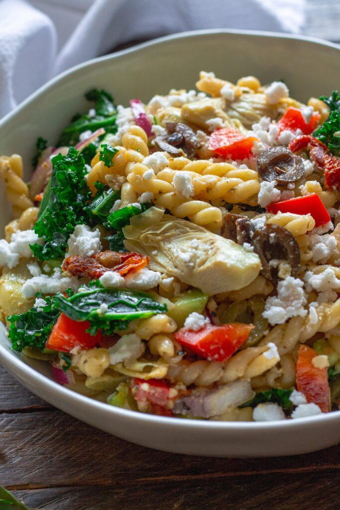 Finished Vegan Mediterranean Pasta Salad garnished with vegan feta crumbles and fresh basil leaves.