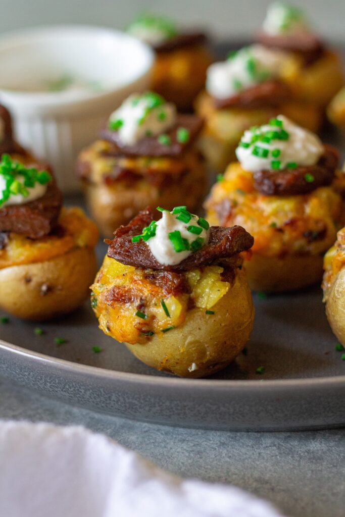 Plate of vegan steak ‘n’ potato bites served with a small bowl of garlic horseradish dipping sauce, garnished with fresh chives.