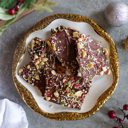 A festive plate of Christmas Cracker Toffee topped with crushed peanuts, sprinkles and sea salt, perfect for holiday celebrations.