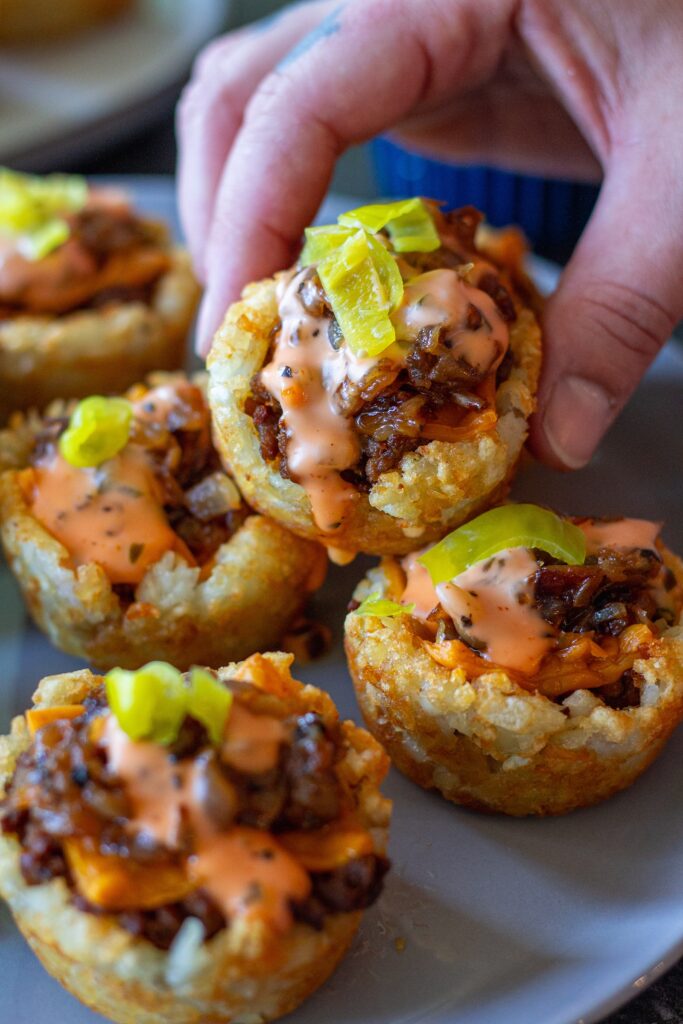 A close-up view of a single tater tot bite showcasing the crispy edges, seasoned filling, and vibrant toppings.