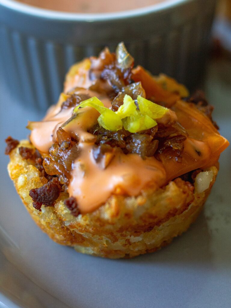 A close-up view of a single tater tot bite showcasing the crispy edges, seasoned filling, and vibrant toppings.