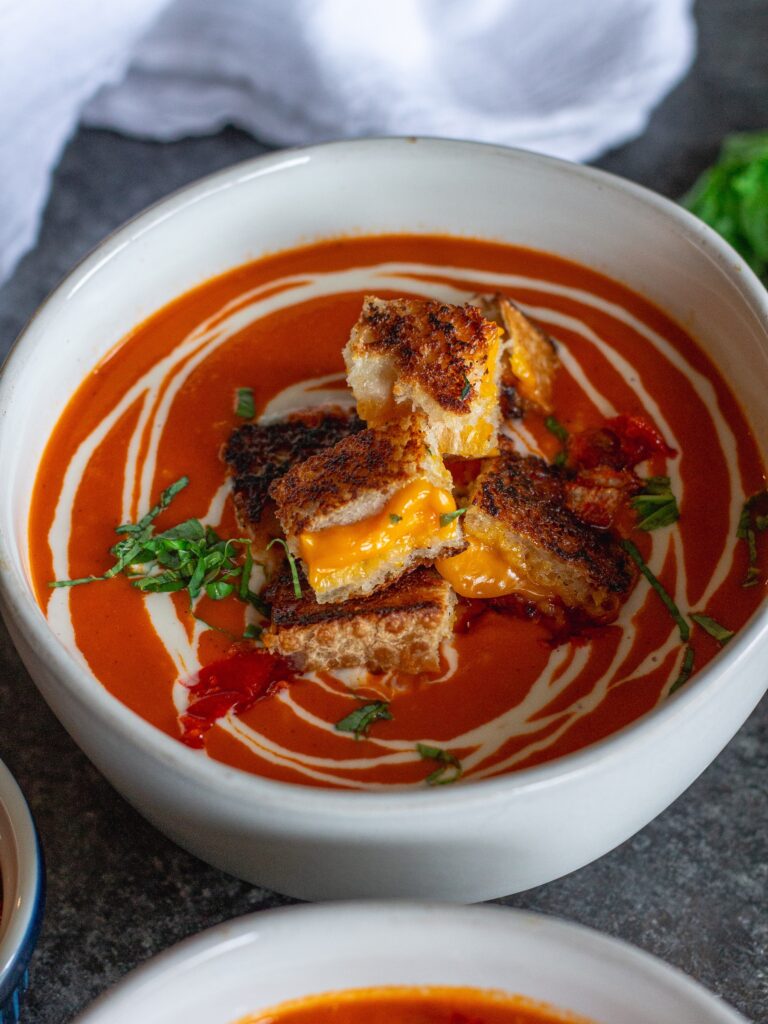 Bowl of Calabrian Chili Tomato Soup garnished with grilled cheese croutons and fresh basil.