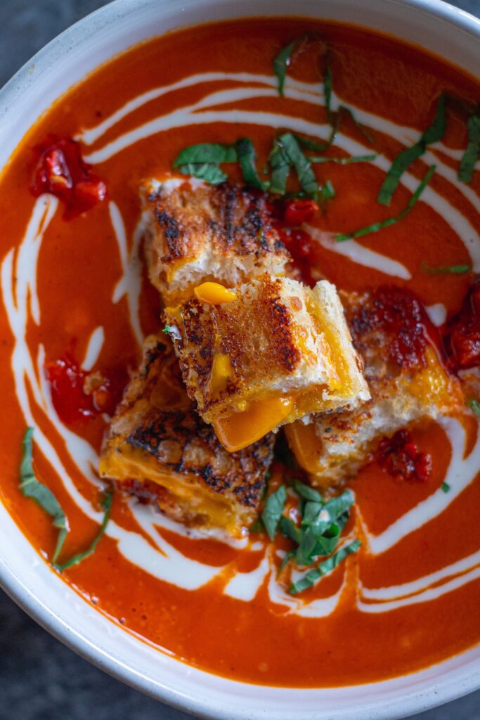 Bowl of Calabrian Chili Tomato Soup garnished with grilled cheese croutons and fresh basil.