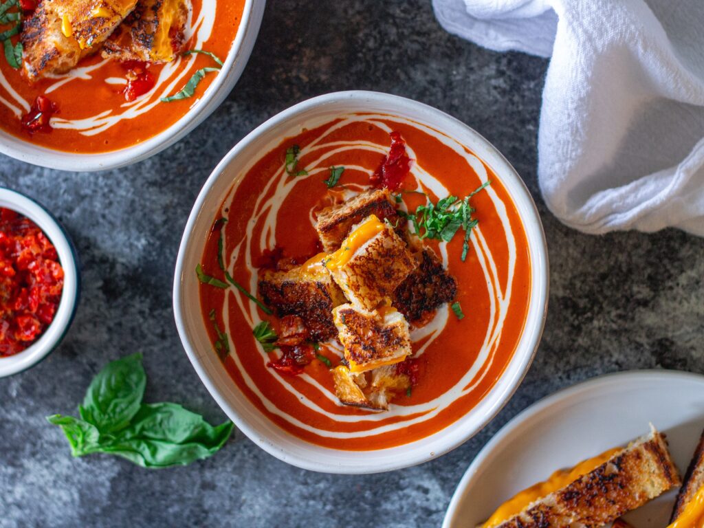 Bowl of Calabrian Chili Tomato Soup garnished with grilled cheese croutons and fresh basil.
