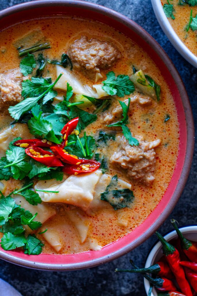 A bowl of Deconstructed Curry Wonton Soup with vibrant curry broth, wonton filling, and fresh herbs.