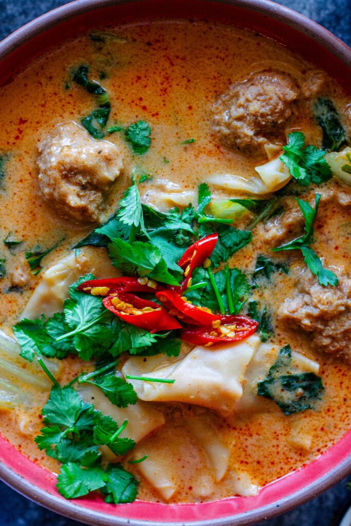 A bowl of Deconstructed Curry Wonton Soup with vibrant curry broth, wonton filling, and fresh herbs.