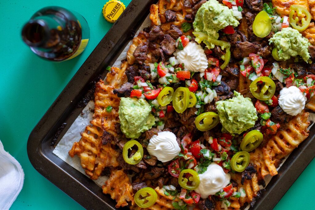Overhead shot of crispy waffle fries loaded with vegan carne asada, guacamole, pico de gallo, and sour cream.