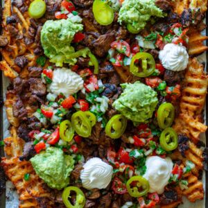 Overhead shot of crispy waffle fries loaded with vegan carne asada, guacamole, pico de gallo, and sour cream.