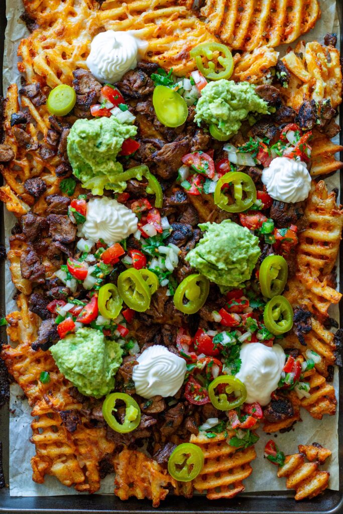 Overhead shot of crispy waffle fries loaded with vegan carne asada, guacamole, pico de gallo, and sour cream.