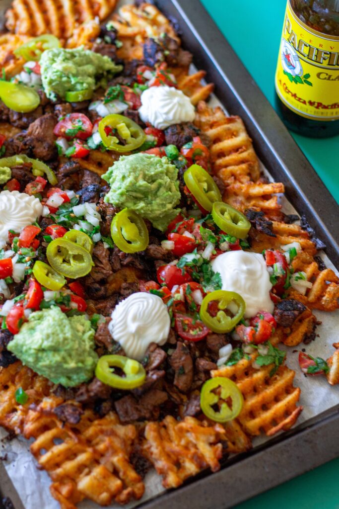 Overhead shot of crispy waffle fries loaded with vegan carne asada, guacamole, pico de gallo, and sour cream.