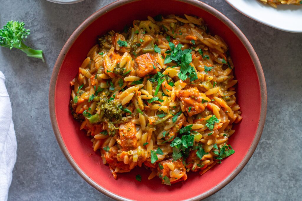 A creamy bowl of broccoli cheddar orzo garnished with fresh parsley.