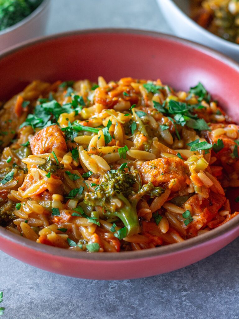 A creamy bowl of broccoli cheddar orzo garnished with fresh parsley.