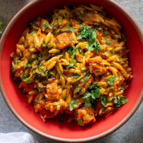 A creamy bowl of broccoli cheddar orzo garnished with fresh parsley.