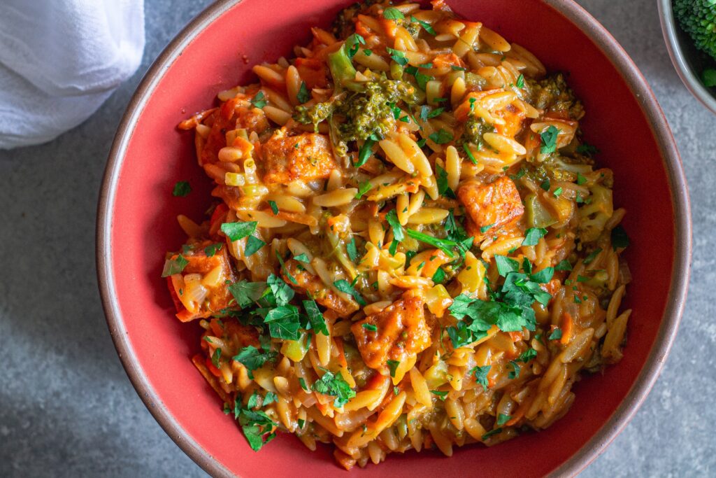 A creamy bowl of broccoli cheddar orzo garnished with fresh parsley.