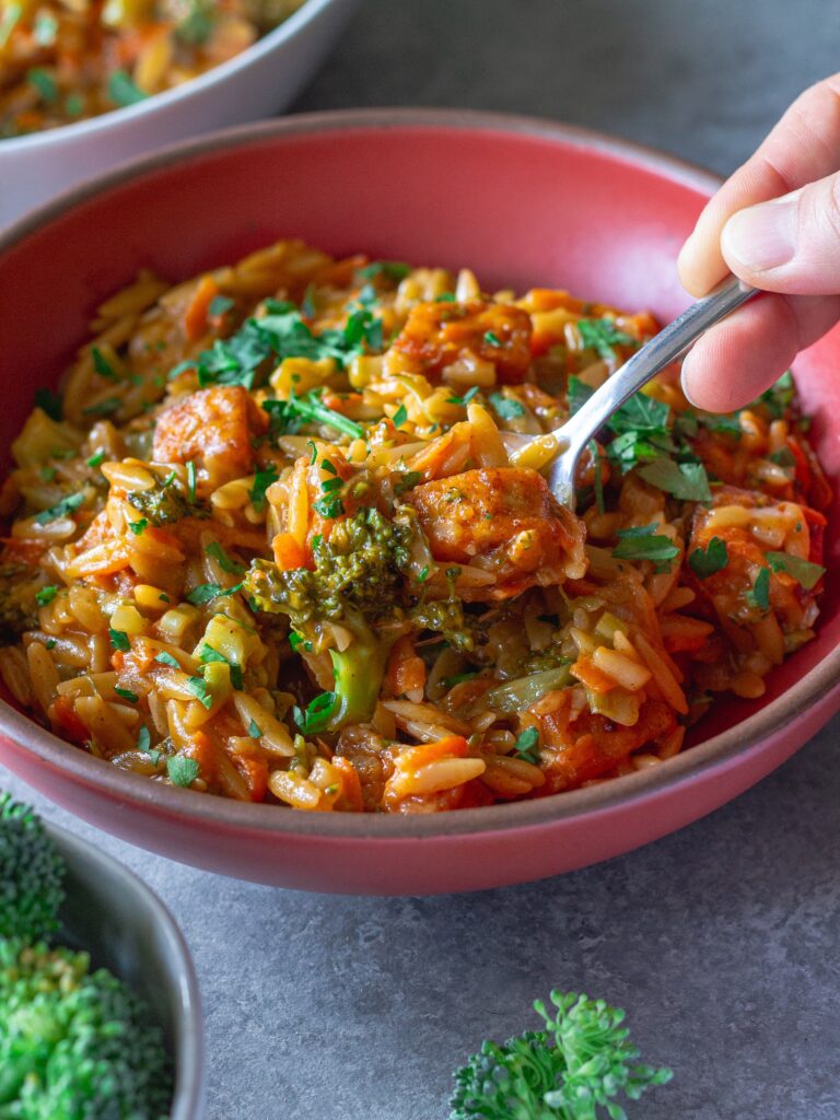 A spoonful of creamy broccoli cheddar orzo lifted from the bowl.